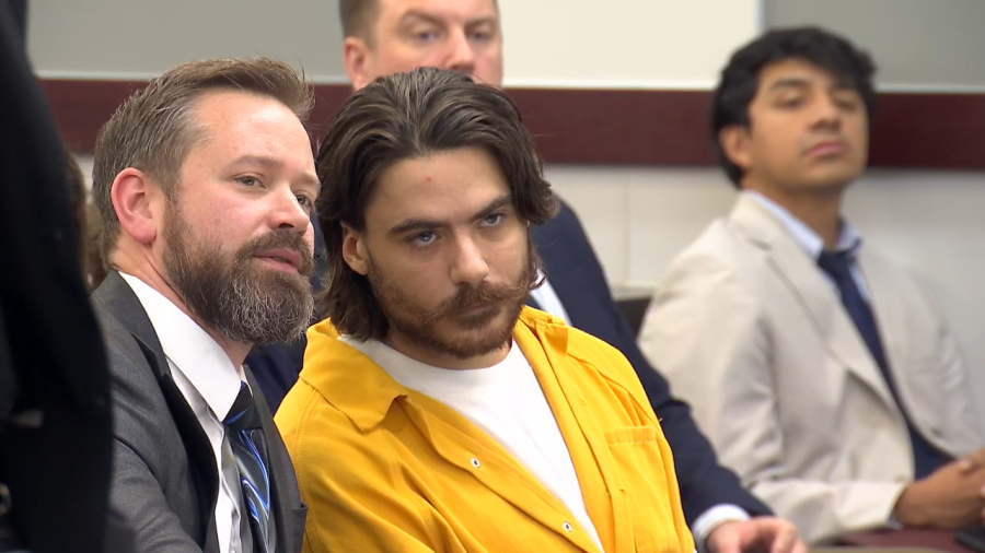 Dalton Eatherly in a yellow jail uniform seated beside an attorney in a courtroom.