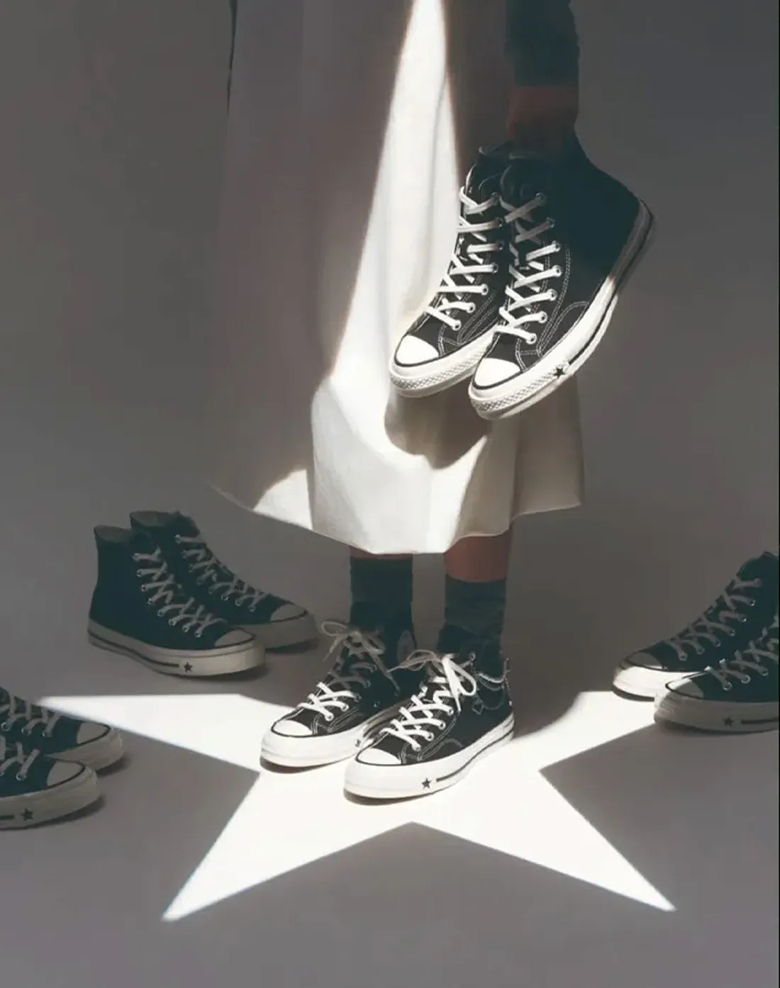 Converse campaign image showing Karina holding black high-top sneakers in a star-shaped field of light.